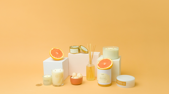 grapefruit mangosteen candles and reed diffusers with grapfruits and mangosteen around the products on orange background